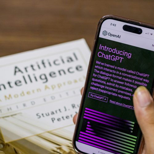 pexels-photo-16461434-16461434 Close-up of a smartphone displaying ChatGPT app held over AI textbook.